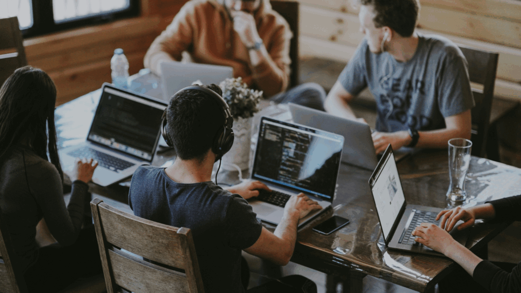 A group of diverse individuals seated at a table, each using a laptop for collaborative work or discussion.