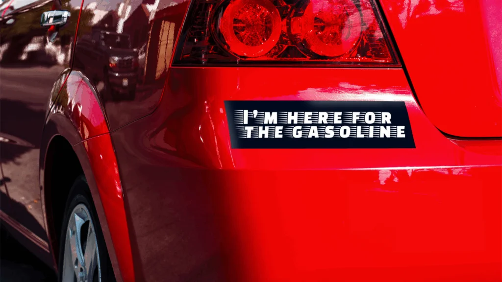 A red car with a bumper sticker that reads, "I'M HERE FOR THE GASOLINE" in white on a black background.