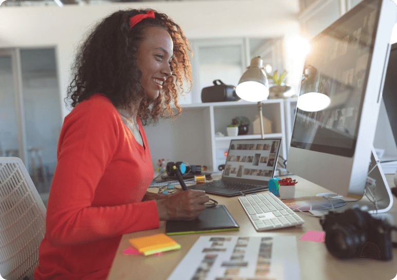 A woman in a red shirt editing a photo on her desktop computer.