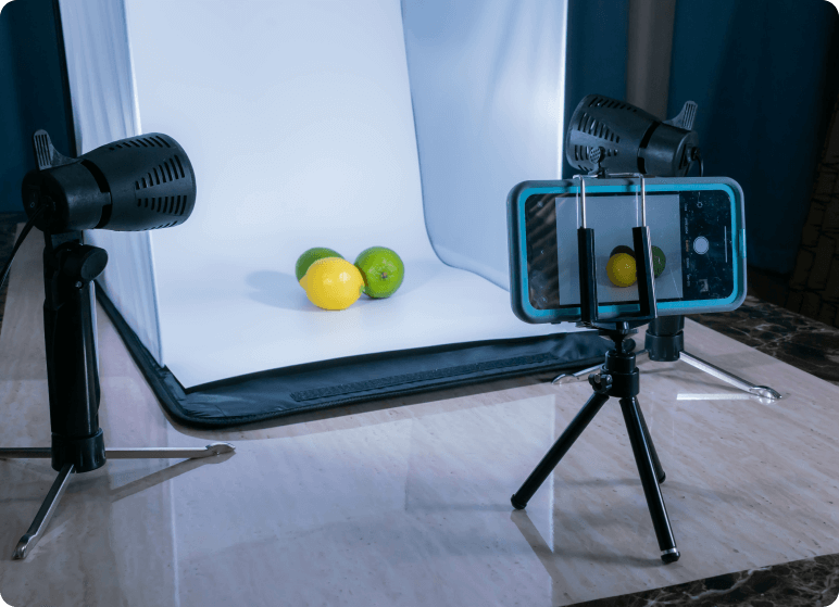 Two lemons and one lime inside a portable photo background. A phone is set on a tripod with a small light next to it, ready to take the photo.