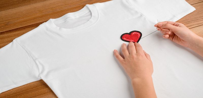A person embroidering a red heart on a white t-shirt by hand.