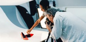 Two people taking a professional photo of red stiletto shoes.