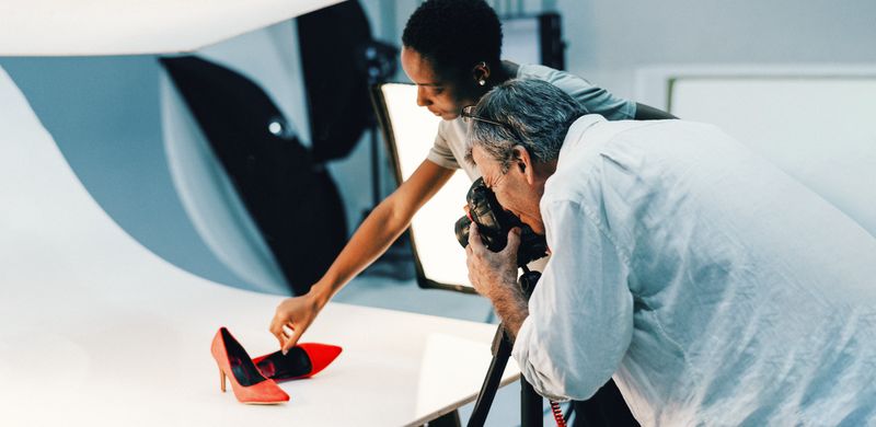 Two people taking a professional photo of red stiletto shoes.