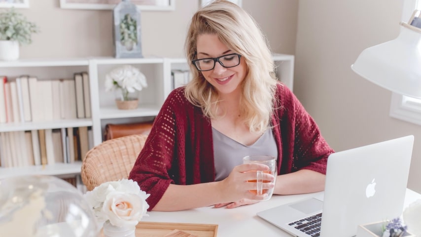 A woman works at her home office while drinking a cup of tea.