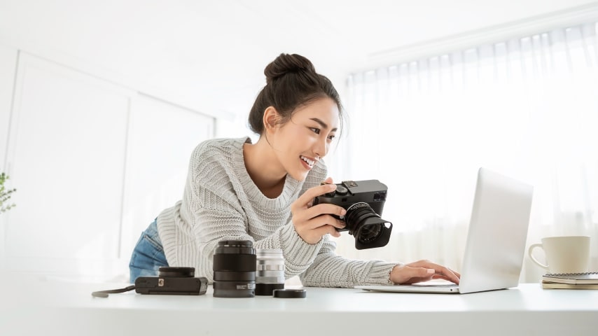 A woman transfers photos from her professional camera to her laptop at home.