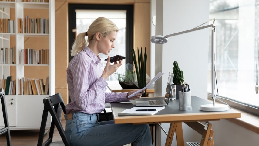 A woman works in her home office while taking a call from a client.