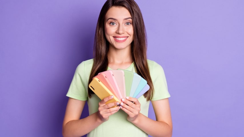 A woman in a green shirt holds eight phone cases in different pastel colors.