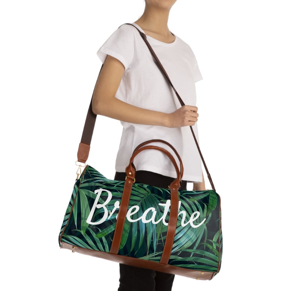 Person with a travel bag over their shoulder that has a design of green leaves and the word “Breathe” printed on it.