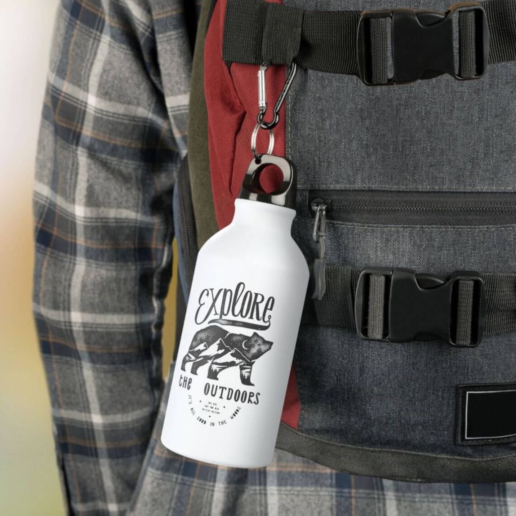 A hiker with a water bottle attached to their bag with a design of a bear silhouette and the text: “Explore the Outdoors.”