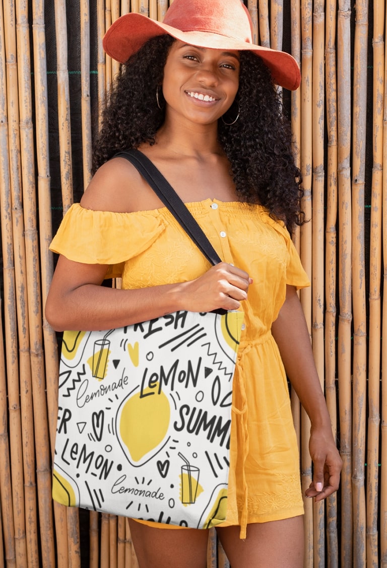 Woman with a tote bag that has a print of stylized lemonade glasses, lemons, and the words “Fresh,” “Lemon,” and “Summer.”