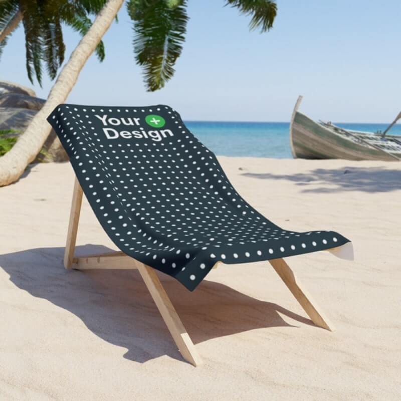 Black Towel with a “Your Design Here” sign placed on a beach chair next to a palm tree near the sea.
