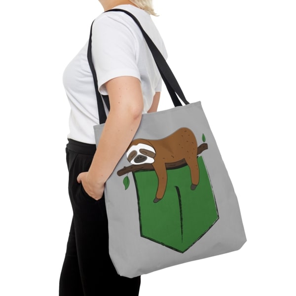 A gray tote bag with a design of a sleeping cartoon sloth on a tree branch.