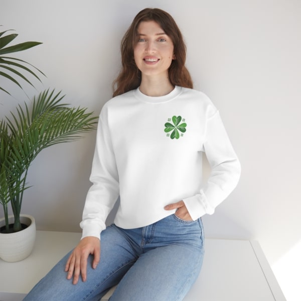 A model wearing a white sweatshirt with a green four-leaf clover design on the top-left side of the chest.