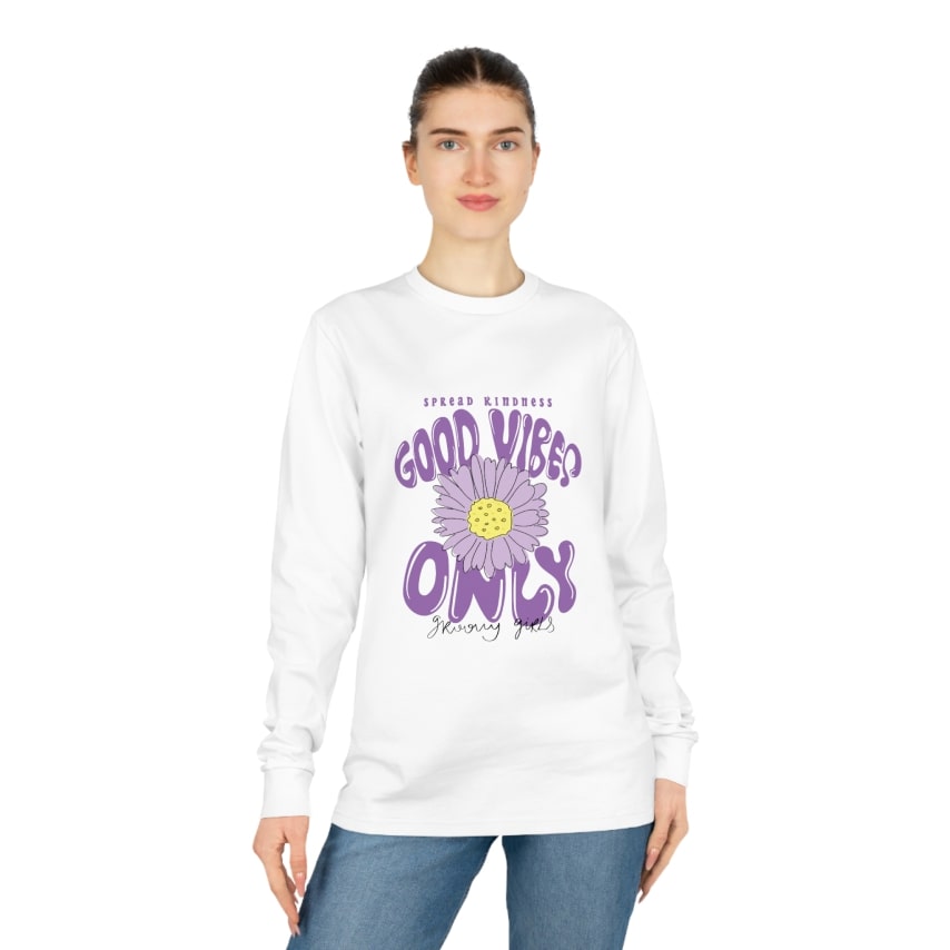 A woman wearing a white long-sleeve t-shirt with a custom print that says "Good Vibes Only".