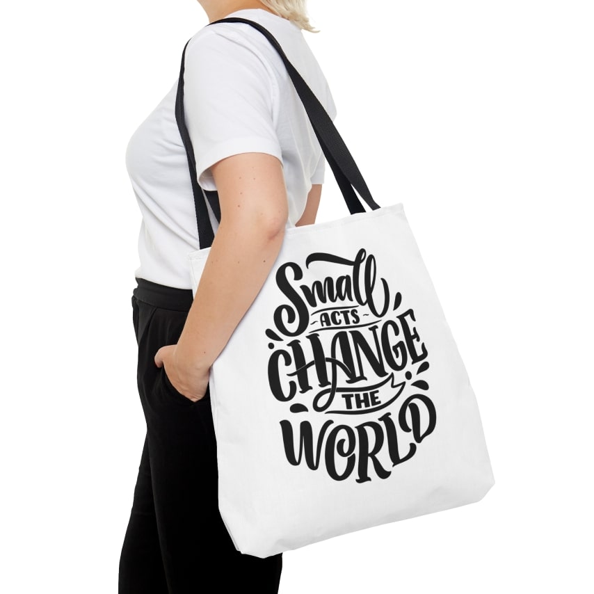 A woman carrying a white tote bag that says "Small Acts Change the World".