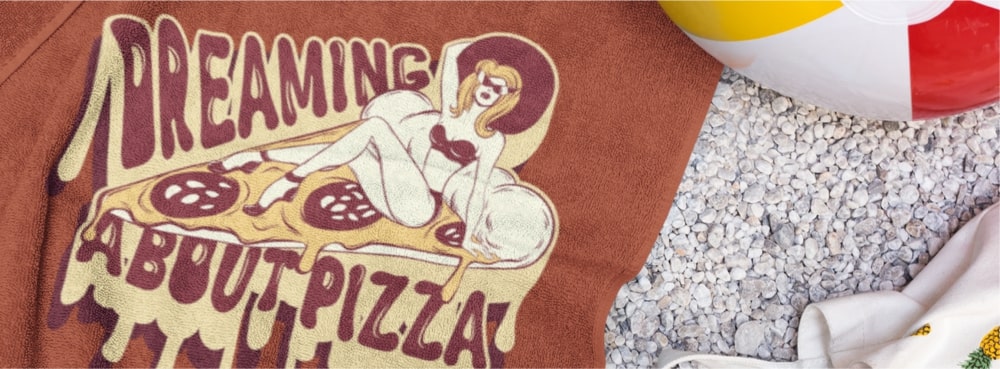 A beach towel with an image of a model in a swimsuit on a pizza slice and the text “Dreaming About Pizza.”