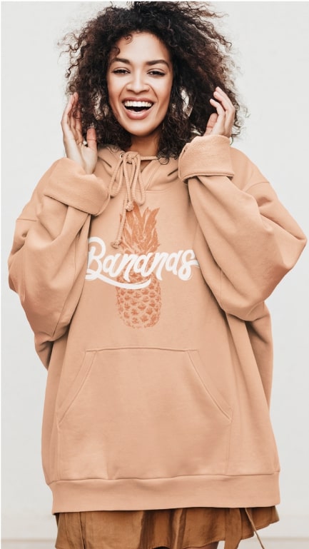 A woman proudly showing off her over-sized brown hoodie with the word "Bananas" written on it and a picture of a pineapple