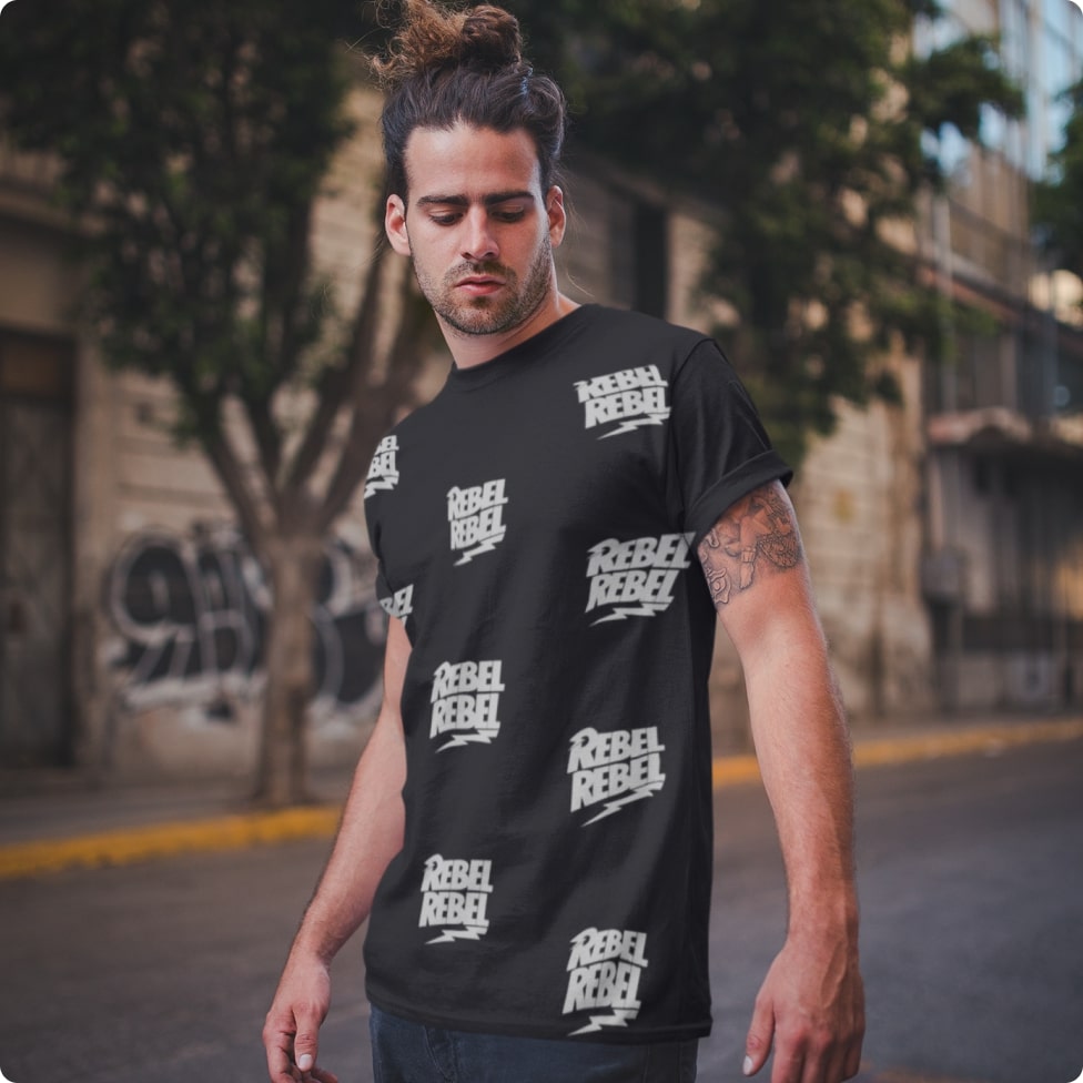 A man in a black all-over-print t-shirt that has a pattern repeating the word "Rebel"