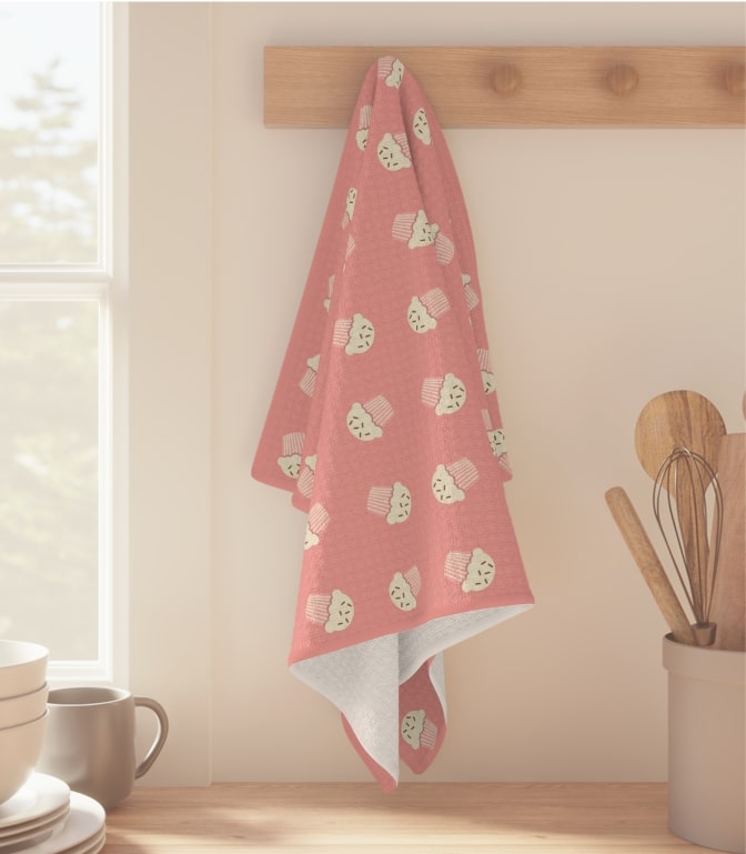 Pink personalized kitchen towel with a pattern of stylized muffins.
