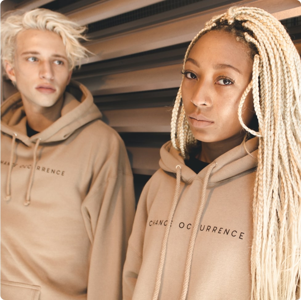A woman and a man posing in cream-colored unisex hoodies that say "Chance occurance"