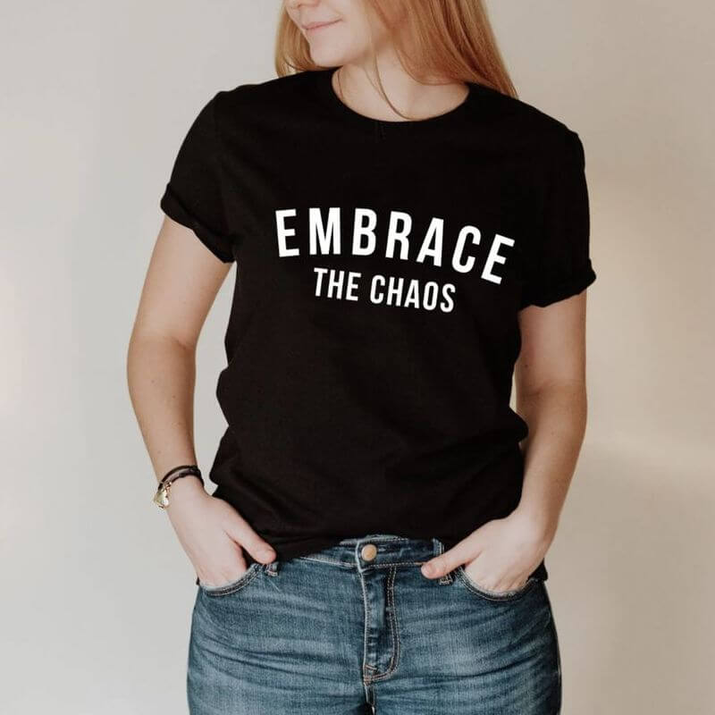 A woman posing in a black t-shirt that says "Embrace the chaos"
