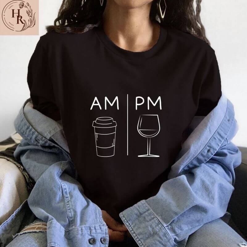 Woman posing in a black t-shirt that has a clever design –AM and a coffee cup, PM and a wine glass