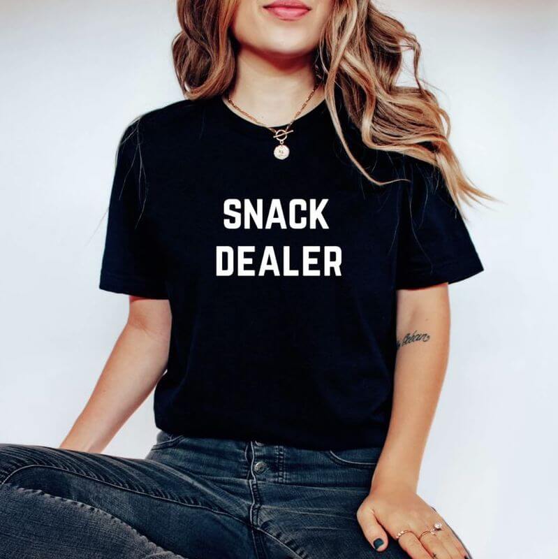 Woman posing in a black t-shirt that says "Snack Dealer"