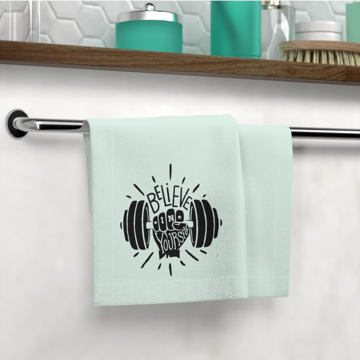 Mint green hand towel with an image of a hand holding a dumbbell and the text “Believe in Yourself.”