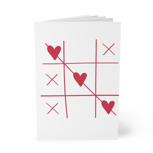 White notebook with a red Tic-Tac-Toe game grid that has three hearts in a vertical row crossed over with a line.