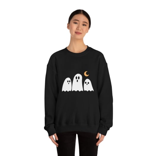 Woman wearing a black sweatshirt with a design of three white ghosts under a crescent moon.