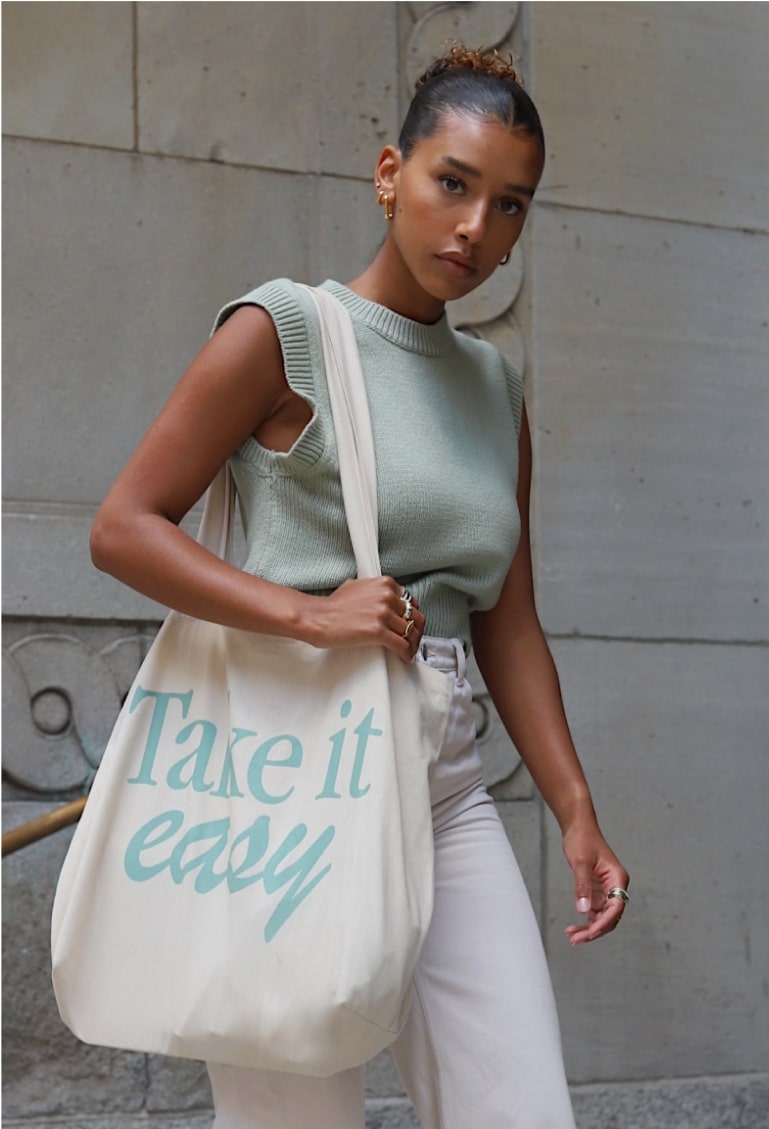 An image of a woman holding a custom tote bag with text on her shoulder.