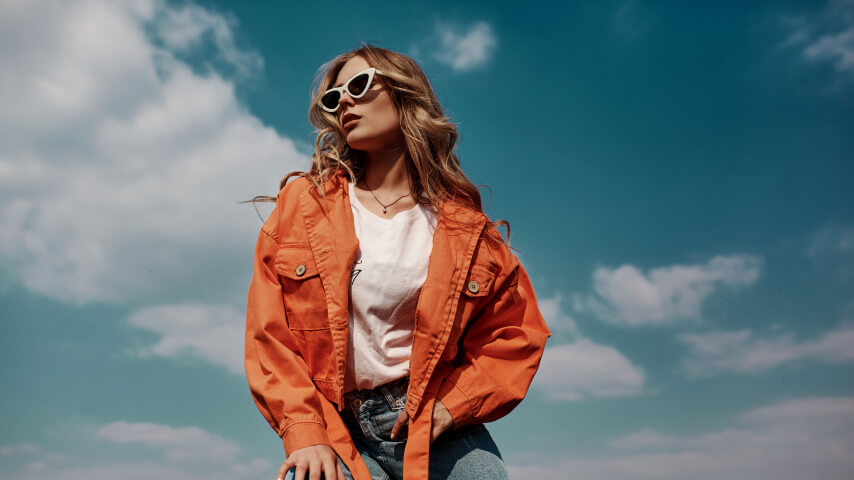A woman posing in a stylish orange jacket and sunglasses.