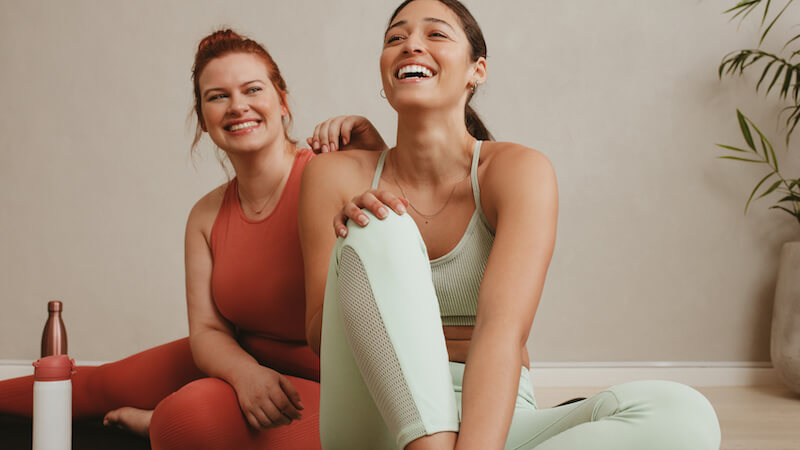 Happy and healthy women laughing in colorful workout outfits, enjoying yoga in style