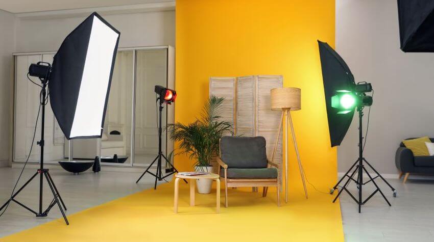A photo set with some furniture on a bright orange background, surrounded by photography lighting equipment.