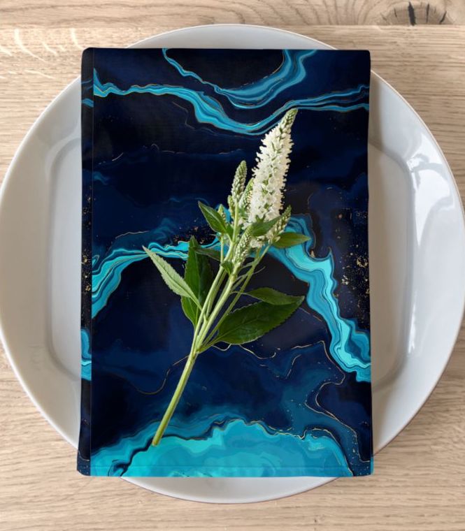A microfiber napkin customized in bluish shades covered by a floral twig over a white ceramic plate on a wooden table