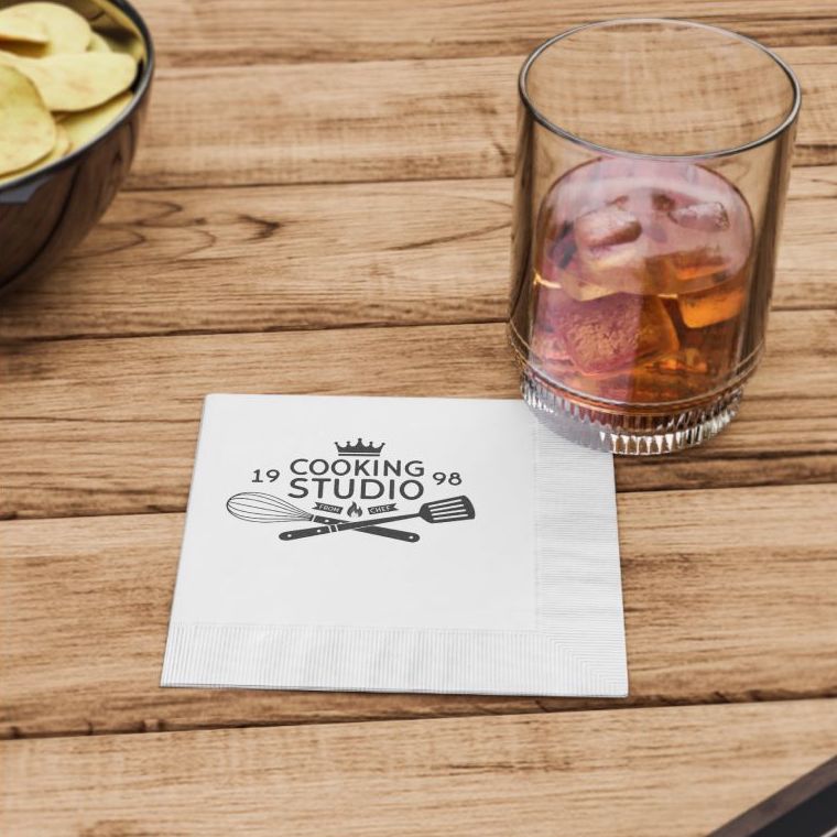 A white paper napkin customized with a restaurant logo, under a cup with a brown soft drink on a wooden table