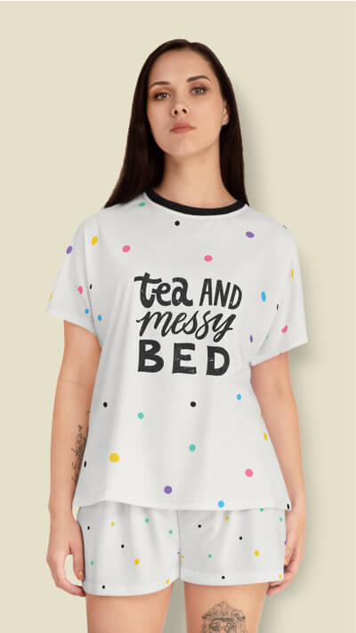 Woman in a white pajama set with a pattern of colorful scattered dots and the text “Tea and messy bed” printed on the shirt.
