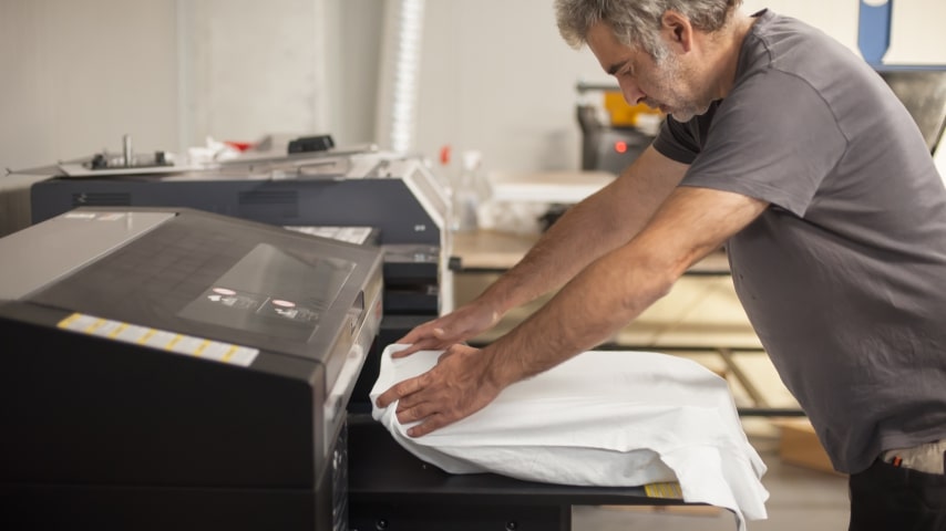 A man placing a white t-shirt in a direct-to-garment ink jet printer.