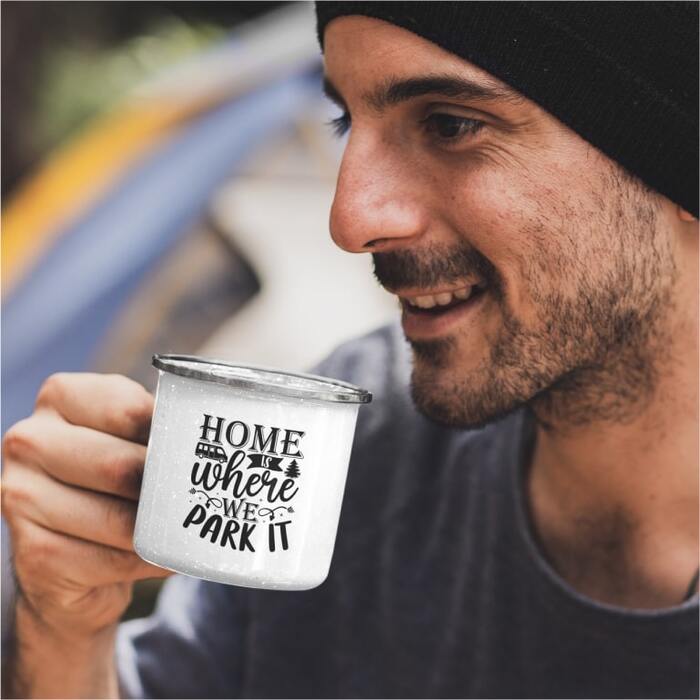 Man holding a camp mug with a design of a tiny van and the text “Home is where we park it.”