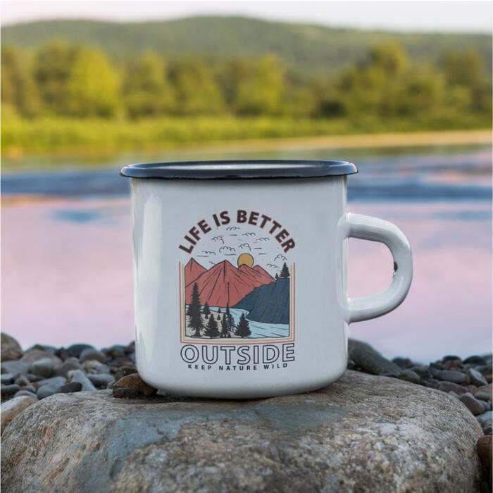 Custom camping mug placed in front of a lake with a scenic imagery design and the text “Life is better outside. Keep nature wild.”