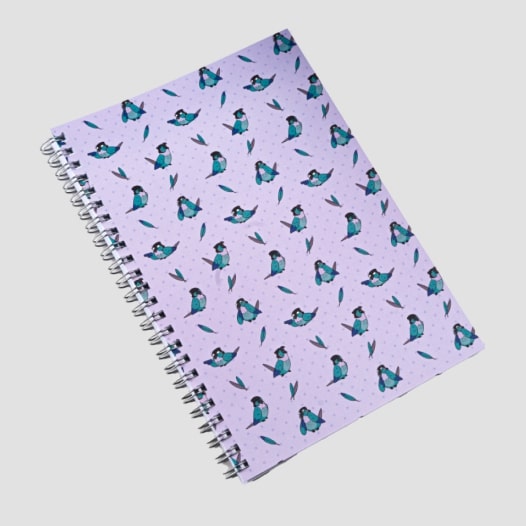 A lilac notebook with a pattern of small blue parrots and feathers.