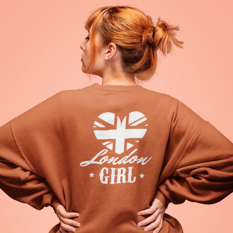 Woman in an orange sweatshirt with the text “London Girl” and a design of the UK flag in the shape of a heart.