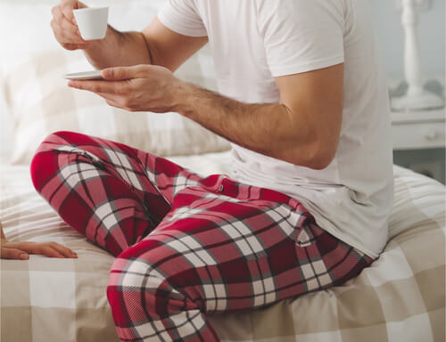 Man sitting in a white shirt and red, gray and white plaid-print pajama pants.
