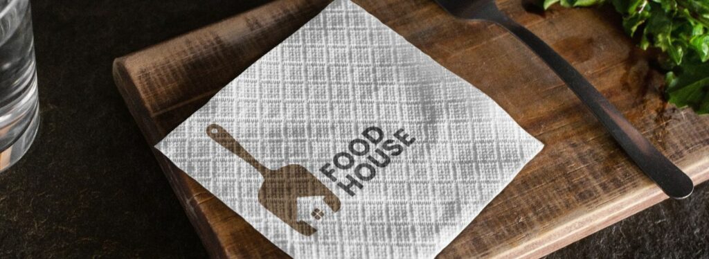 A white paper napkin customized with a restaurant logo over a cutting board beside a spoon and parsley twigs