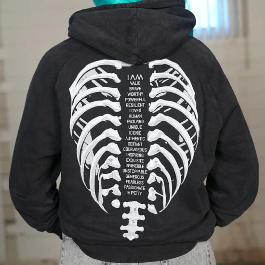 A black hoodie with a rib cage design on the back and a list of adjectives in the middle.