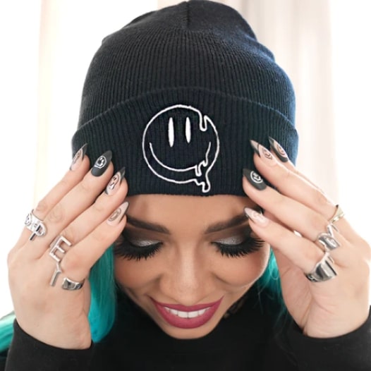 A woman wearing a black beanie with a melting smiley face design.