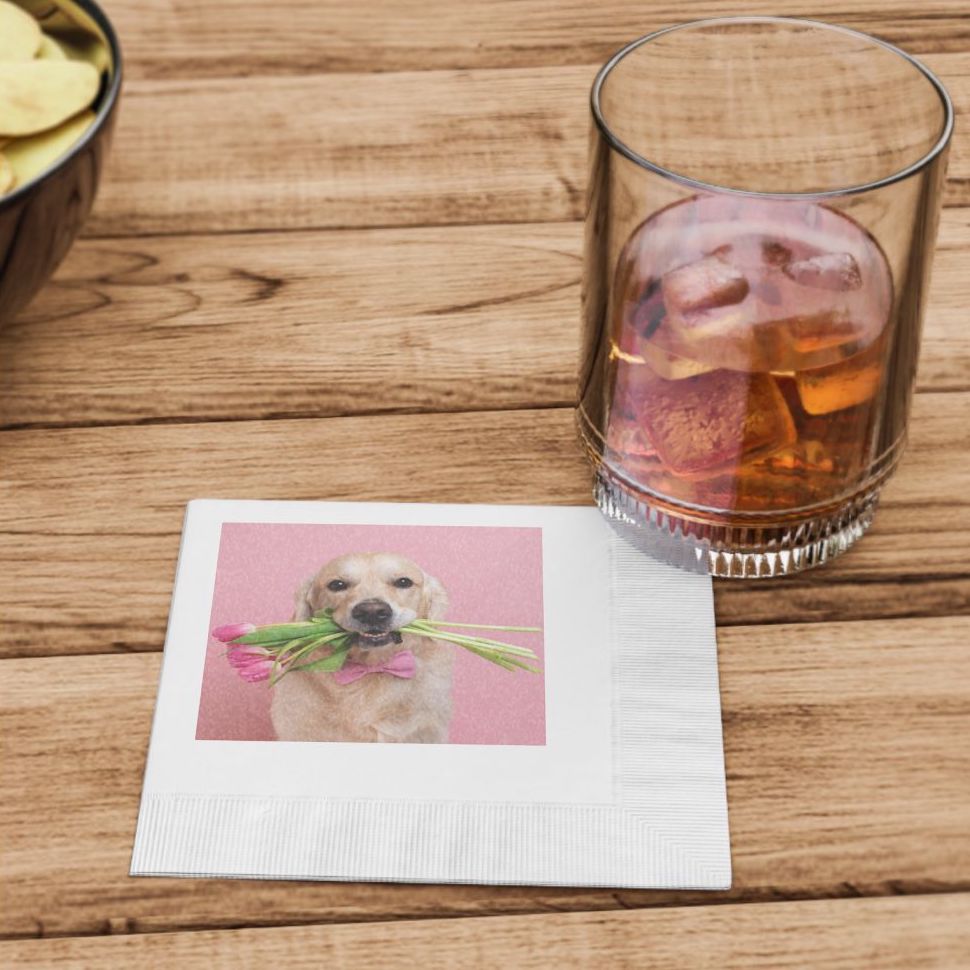 A white paper napkin customized with a labrador picture under a cup with a brownish drink over a wooden table