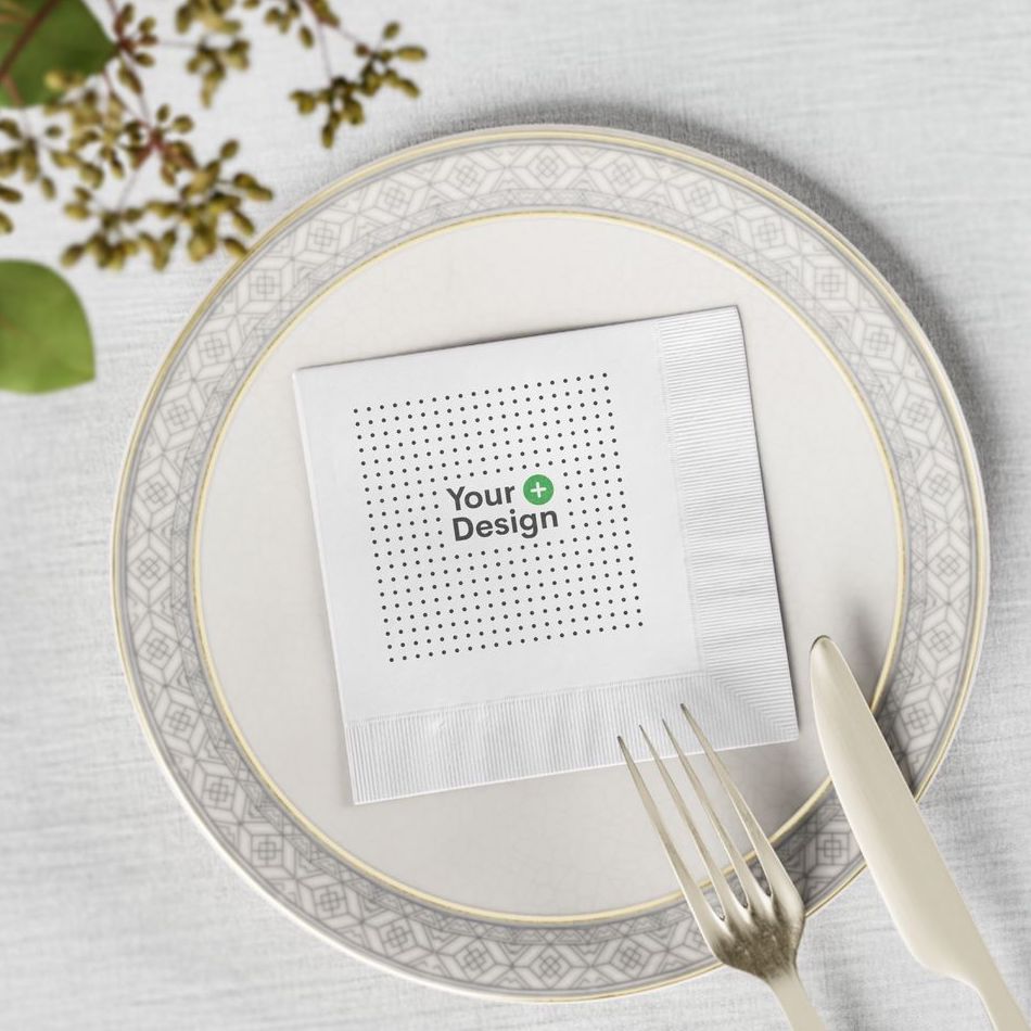 A customizable paper napkin from Printify over a delicate round plate on a white table with small twigs