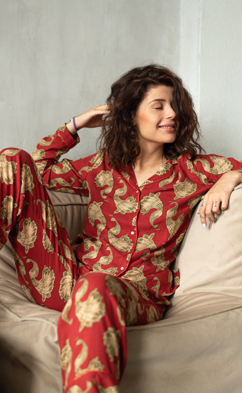 Woman lounging in a set of red satin pajamas with a pattern of golden ornaments.
