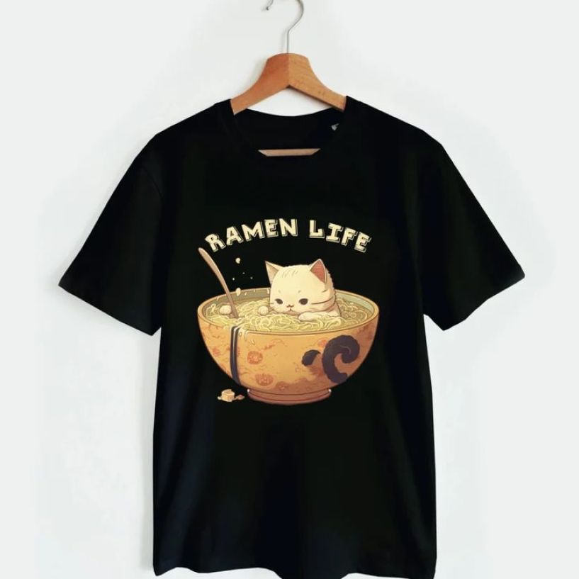 یک تی شرت مشکی با یک گربه کارتونی به سبک ژاپنی نارنجی رنگ که در یک کاسه بزرگ سوپ رامن شنا می کند و عبارت «رامن زندگی» روی قسمت سینه نوشته شده است.